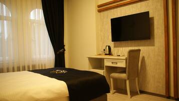 Habitación de hotel con cama, escritorio, silla, televisor montado en la pared y ventana con cortinas.