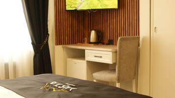 A hotel room with a bed, a desk, a chair, a television mounted on a wooden panel, and a wardrobe.