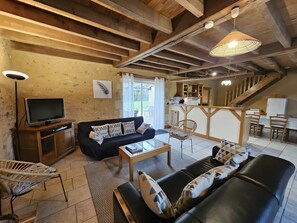 Una sala de estar acogedora con sofá, televisión, comedor con sillas, cocina y escalera.