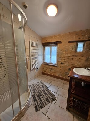 Une salle de bain avec une douche à parois de verre, un meuble-lavabo en bois avec un évier, un mur en pierre et une petite fenêtre.