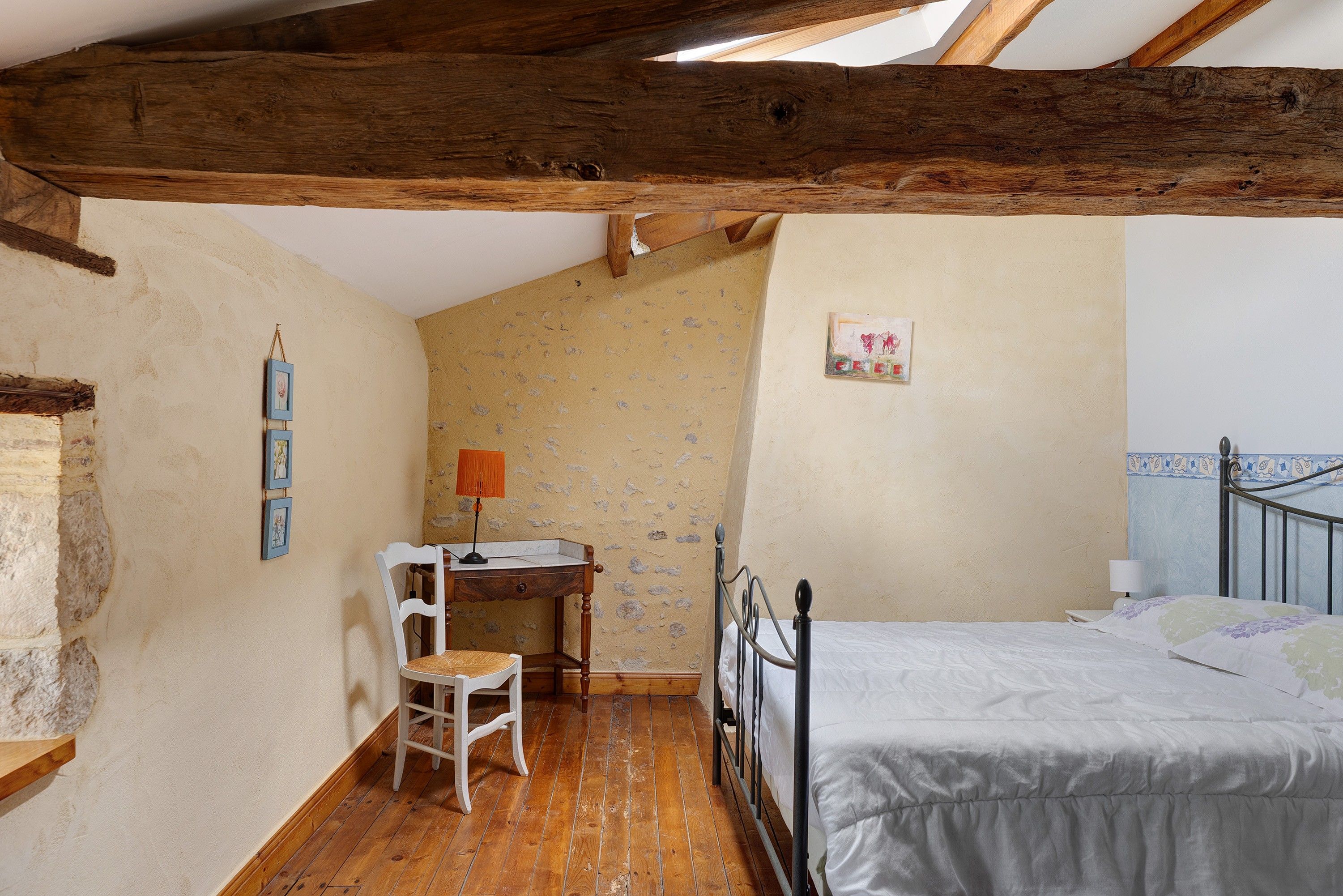 Ein Schlafzimmer mit Holzboden, einem Bett, einem Schreibtisch mit Stuhl und einem kleinen Tisch mit Lampe.