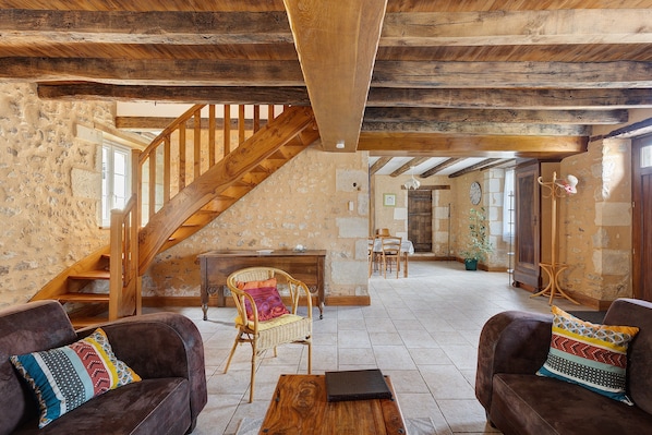 A rustic interior with exposed wooden beams, a stone fireplace, and a dining area.
