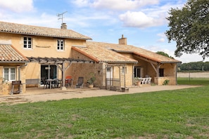 Ein zweistöckiges Haus mit einem Ziegeldach, einer Terrasse mit Gartenmöbeln und einem Rasen.