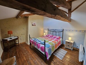 Un dormitorio con cama, mesitas de noche, escritorio, silla y radiador.