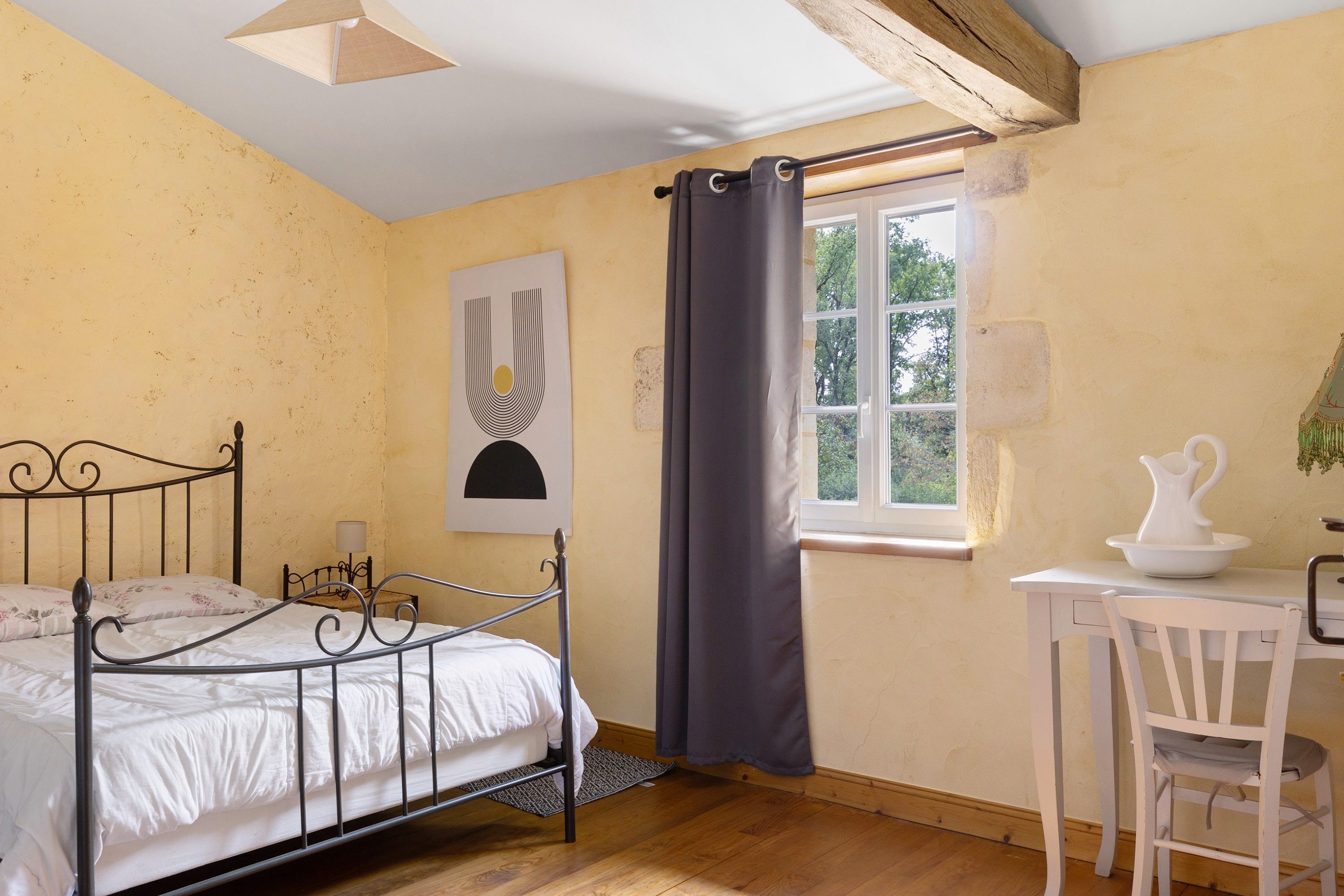 Une chambre à coucher comprenant un lit, un bureau, une chaise, une fenêtre avec des rideaux et un tableau accroché au mur.