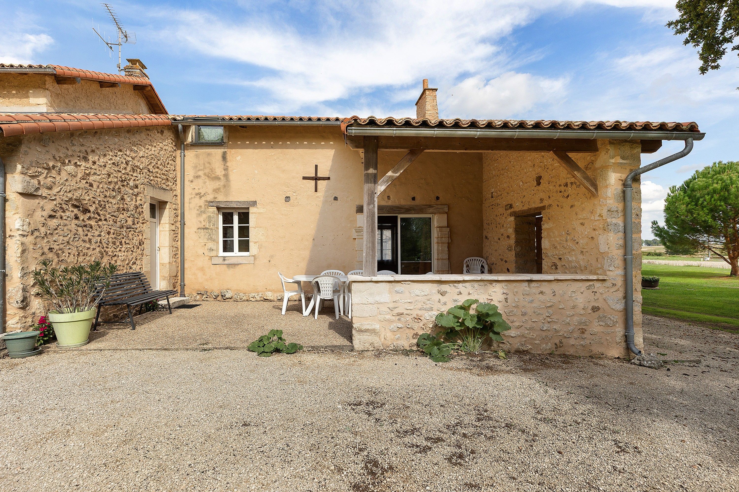Un bâtiment rustique à la façade en pierre, surmonté d’une croix, et doté d’un petit patio avec une table et des chaises.