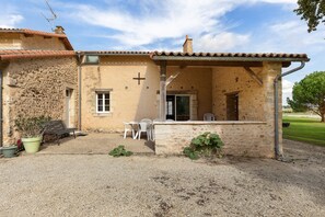 A rustic building with a stone facade, a cross, and a small patio with a table and chairs. - Le Refuge des Oiseaux: Shared Terrace, Private Garden & Wi-Fi in Lusignan (Lusignan)