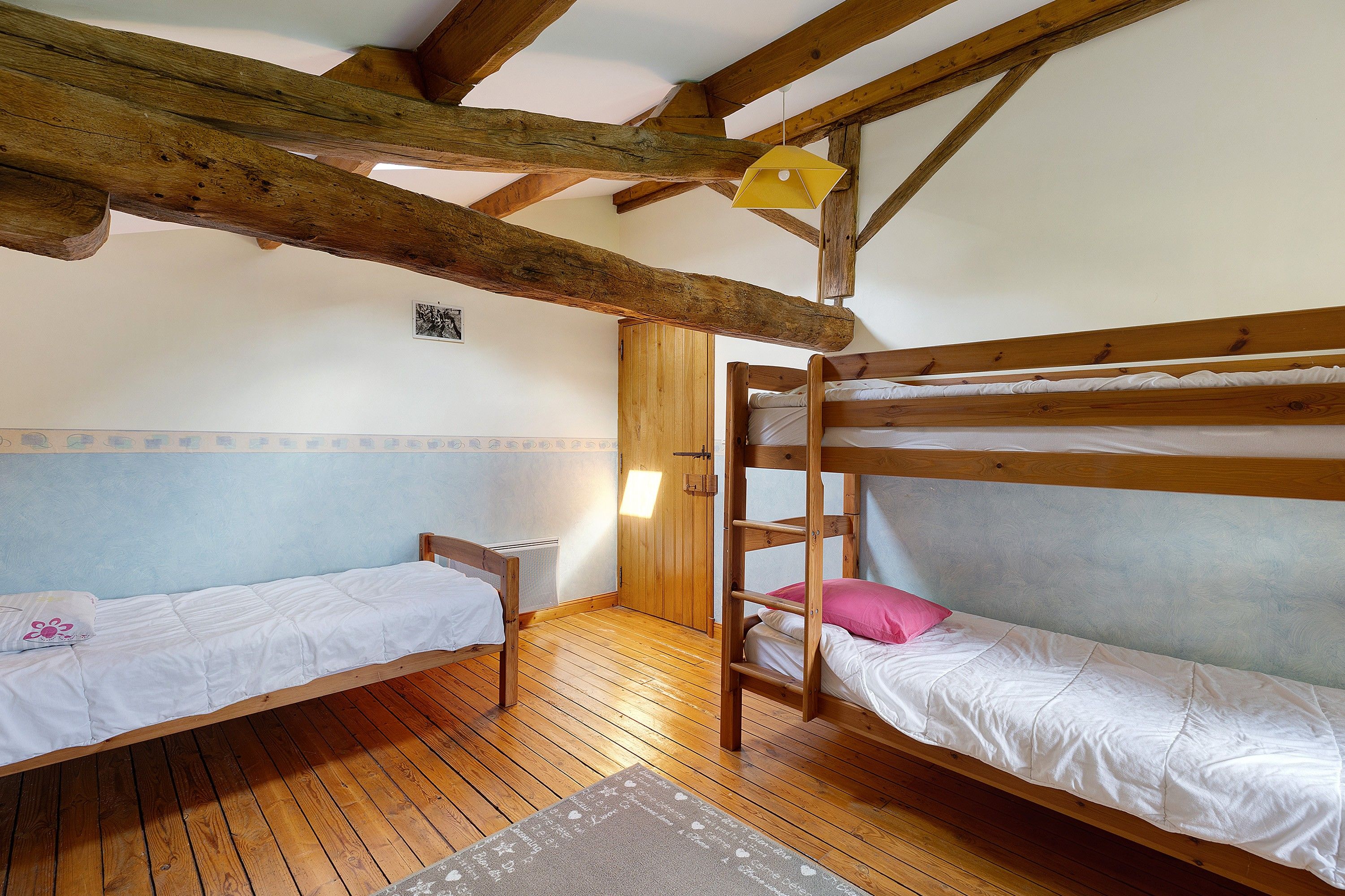 Une pièce avec deux lits superposés, des poutres en bois au plafond, une petite table et une porte.