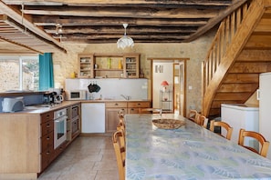 A rustic kitchen with wooden beams, a dining table, and basic appliances.