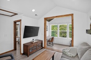 Ein Wohnzimmer mit Fernseher, Holzmöbeln, einem Fenster mit Blick und einer Tür zu einem anderen Raum.