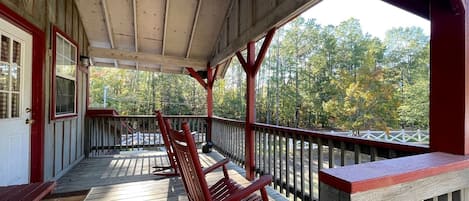 A covered porch with wooden railings and benches, overlooking a forested area.