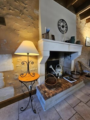 Una chimenea con un reloj encima, una mesa con una lámpara al lado y una cesta en la repisa.