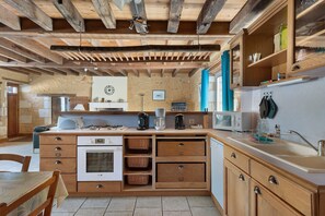 Een keuken met houten kasten, een inbouwoven en een eethoek met een tafel en stoelen.