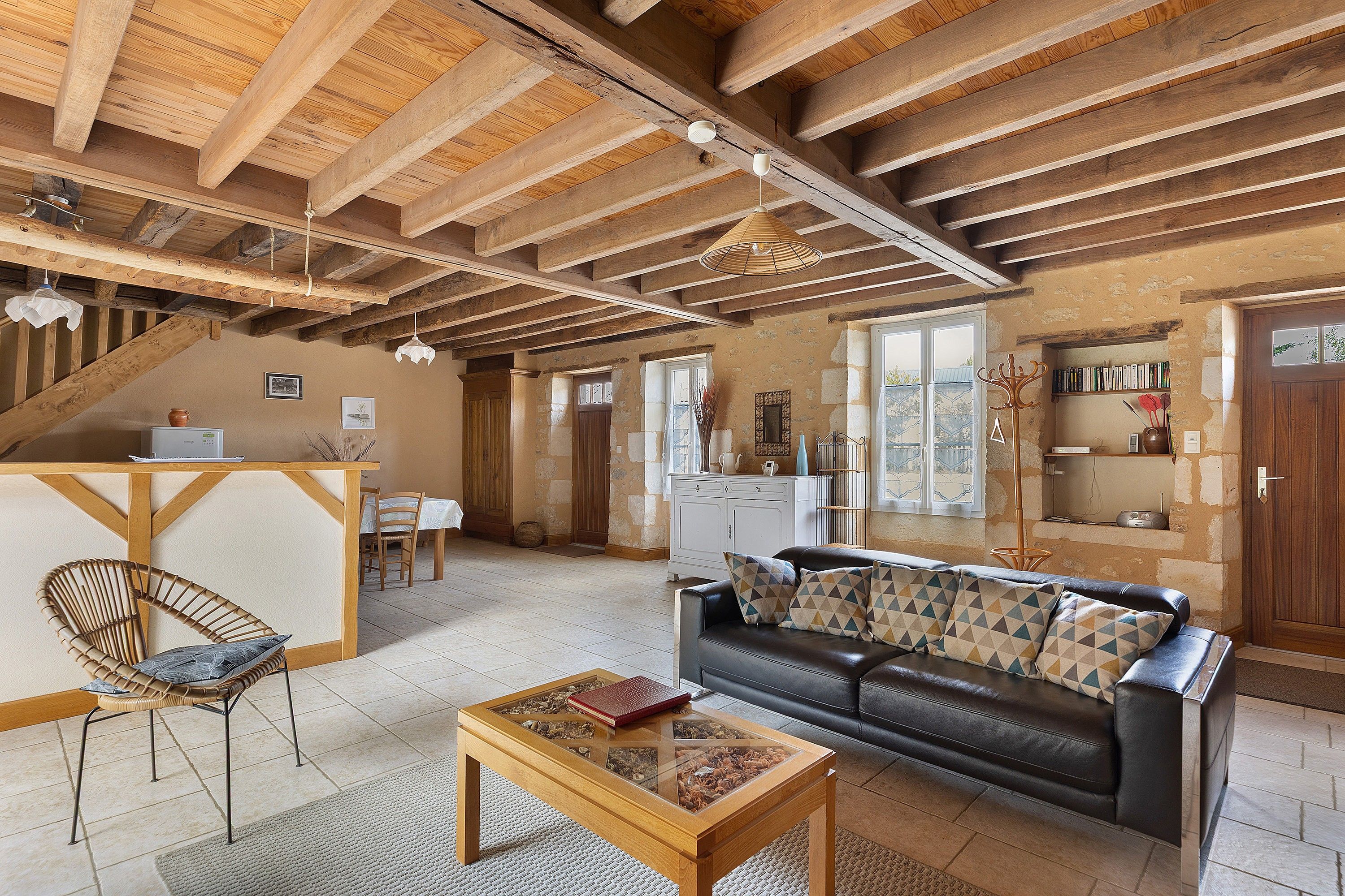 Un vaste espace de vie doté d’un haut plafond en bois, d’un canapé en cuir, d’une table basse en bois et d’un fauteuil en osier.