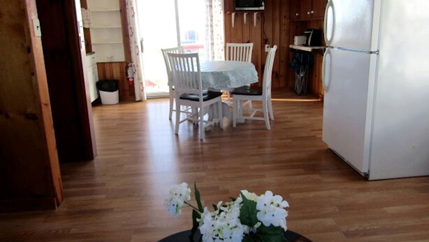 Une cuisine avec des meubles de rangement en bois, un réfrigérateur blanc, une table à manger avec des chaises et un arrangement floral sur la table.