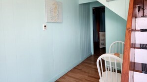 Un couloir aux murs bleu clair, avec un plancher en bois, une chaise blanche et une porte donnant sur une autre pièce.