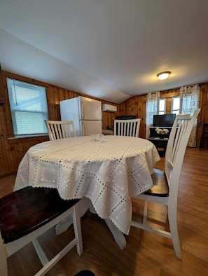 A dining area with a round table, white chairs, and a refrigerator in the background.