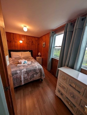 A wooden-paneled room with a bed, dresser, and window with curtains.