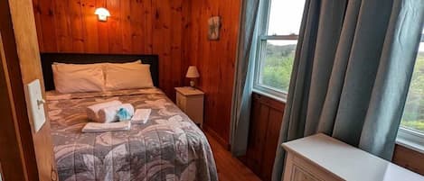 A wooden-paneled room with a bed, dresser, and window with curtains.