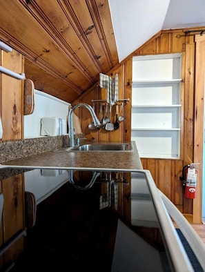 A compact kitchen with wooden walls, a granite countertop, and a stainless steel sink.