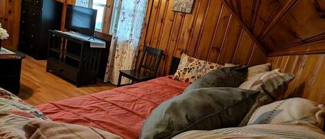 A cozy room with a bed, a dresser, a television, and a window with curtains.