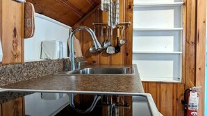 A compact kitchen with wooden walls, a granite countertop, and a stainless steel sink.