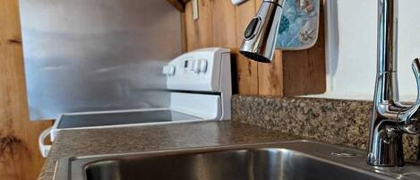 A kitchen with a stainless steel sink, granite countertop, wooden cabinets, and a white stove.