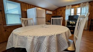 A dining area with a round table, white chairs, and a refrigerator in the background.