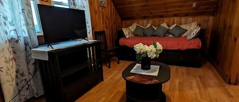 Una habitación con paneles de madera, un televisor, un sofá y una pequeña mesa con flores.