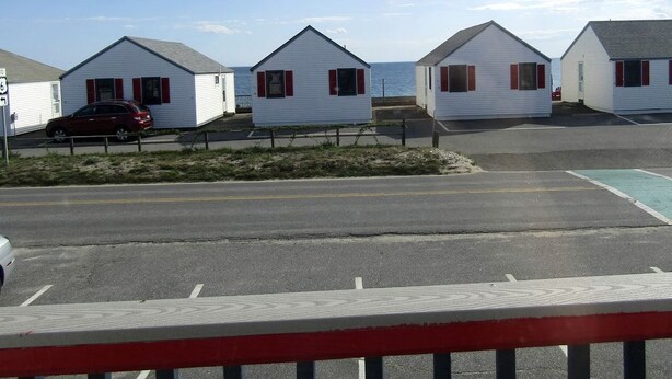 A row of white mobile homes with red trim, a parking lot, and a clear sky.