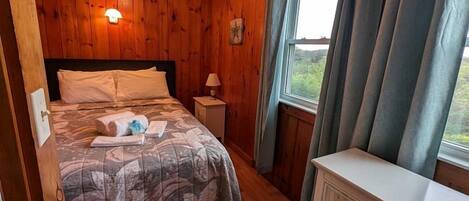 A wooden-paneled room with a bed, dresser, and window with curtains.