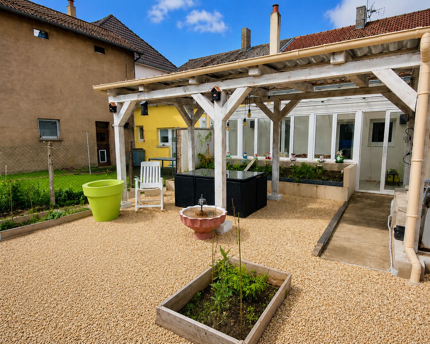 Un patio couvert aménagé avec des sièges, un parterre surélevé et une vue sur un bâtiment jaune.