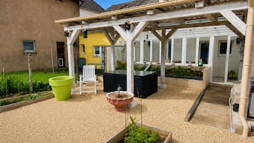 Un patio couvert aménagé avec des sièges, un parterre surélevé et une vue sur un bâtiment jaune.