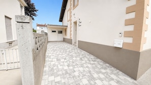 Une ruelle étroite au sol carrelé, un mur de béton sur la gauche et un immeuble aux murs beige et blancs sur la droite.