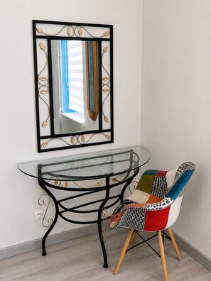 Une table avec un plateau en verre et un cadre en métal noir, une chaise avec un siège à motifs, et un miroir mural orné de motifs de feuilles.