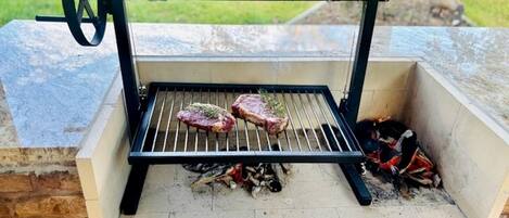 Una parrilla portátil con dos filetes a la parrilla sobre llamas abiertas, frente a un muro de piedra.
