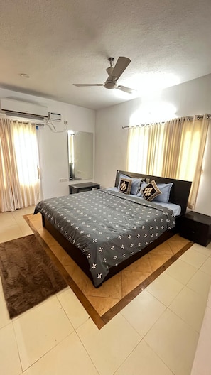 A bedroom with a bed, a ceiling fan, an air conditioning unit, a mirror, and curtains.
