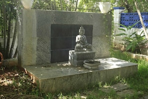 A stone Buddha statue on a pedestal with a water basin in a garden setting.