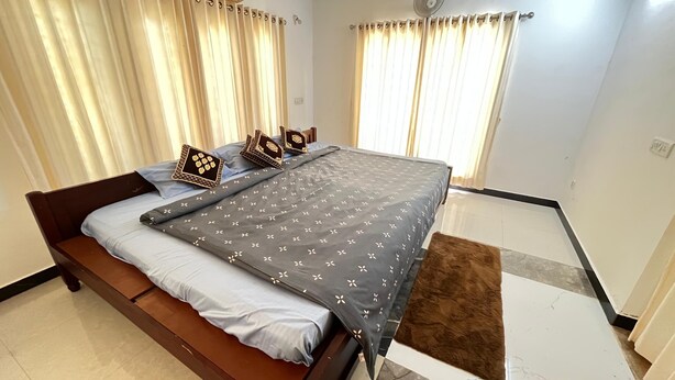 A bedroom with a bed, curtains, a window, and a thermostat. - Hotel Govas (Vadanemmeli)