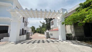 A gated entrance with a white pergola, a paved pathway, and buildings with balconies and windows.