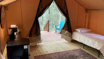 A tent with two beds, a small table with a lamp, and a view of the outdoors.
