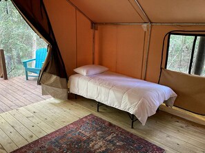 Ein Zelt mit einem Einzelbett, einem Fenster und einer Holzterrasse mit einem Stuhl.