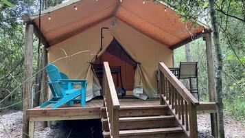 A wooden deck with a tent structure, a chair, and a staircase leading to the tent.