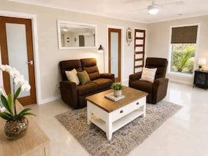 A modern living room with a sofa set, a coffee table, a mirror, and a view of greenery outside.