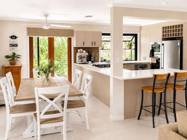 A modern kitchen with a central island, white cabinetry, and a dining area with white chairs.