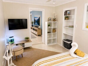 Un dormitorio con cama, escritorio, televisor, estantería y una puerta que da a otra habitación.