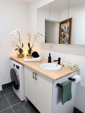 Un baño moderno con lavadora, lavamanos, espejo y toallas.