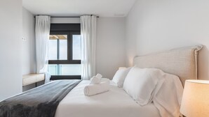 Et hotelværelse med en seng, et natbord, en lampe og et vindue med gardiner.