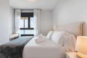 Ein Hotelzimmer mit Bett, Nachttisch, Lampe und einem Fenster mit Vorhängen.