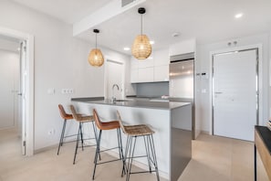 Eine moderne Küche mit einer zentralen Kochinsel, Barhocker, Pendelleuchten und einem Kühlschrank.
